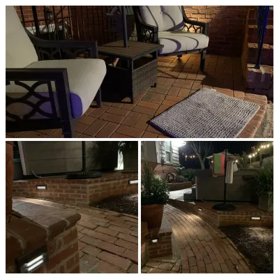 This nighttime view captures a completed outdoor living space featuring red brick paving, patio furniture, a hot tub, and modern low-voltage step lighting integrated into the brick walls.